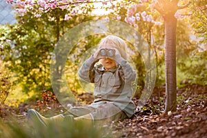 Blonde little toddler child with binoculars, sitting in garden on sunset