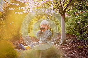 Blonde little toddler child with binoculars, sitting in garden on sunset