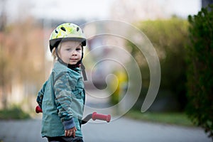 Blonde little toddler child in riding bike, wearing helmet and playing on the playground