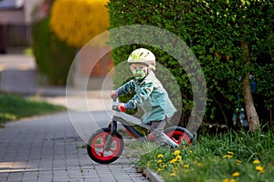 Blonde little toddler child in riding bike, wearing helmet and playing on the playground