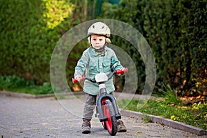 Blonde little toddler child in riding bike, wearing helmet and playing on the playground