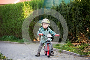 Blonde little toddler child in riding bike, wearing helmet and playing on the playground