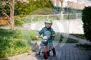 Blonde little toddler child in riding bike, wearing helmet and playing on the playground