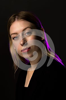 Blonde with long hair in a black suit on a black background, purple light.