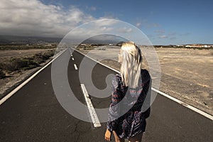 Blonde long hair girl viewed fromback walk on a long straight asphalt road - concept of freedom and independence - hope and future