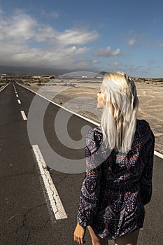 Blonde long hair girl viewed fromback walk on a long straight asphalt road - concept of freedom and independence - hope and future