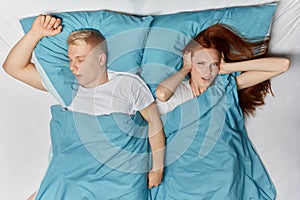 Blonde man snoring and angry ginger woman cannot sleep.