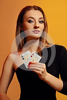Blonde model with bright make-up, in black dress is showing two aces, posing against colorful background. Gambling