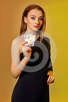 Blonde model with bright make-up, in black dress is showing two aces, posing against colorful background. Gambling