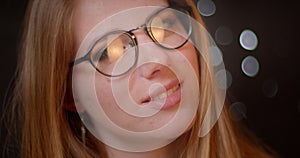 Blonde model with bright make-up in eye-glasses smiling seductively into camera on bokeh background.
