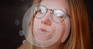 Blonde model with bright make-up in eye-glasses watching seductively into camera on bokeh background.