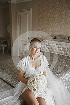 blonde model girl with blue eyes and gentle makeup, in lace peignoir and in white lingerie with the bouquet of