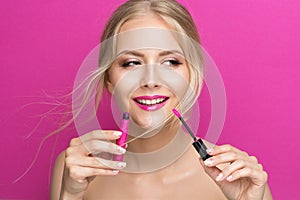 Blonde Model Girl holding Pink Lipstick Brush over Bright Magenta Background. Summer Beauty Woman Face Cosmetics Make up. Fashion