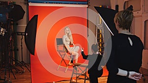 Blonde model girl lying in photo studio - photographer and make up artist straightens hair, fashion backstage