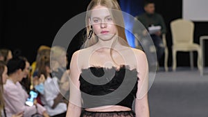 Blonde model girl in transparent dress walks on defile podium. Fashion catwalk.