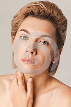 Blonde model with a short haircut and green eyes looks at the camera. Close-up, retouch, shot in the studio on a light