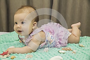 Blonde newborn baby girl in a bathing suit lies on the bed