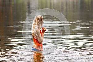 A blonde in an orange wet t-shirt stands waist-deep in water