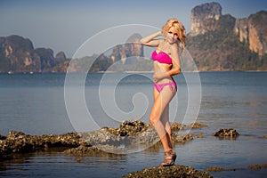 blonde in pink swimsuit on rock in sea