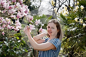 blonde with pleasure inhales an aroman of magnolia flowers standing under a tree