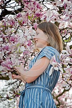 blonde with pleasure inhales an aroman of magnolia flowers standing under a tree