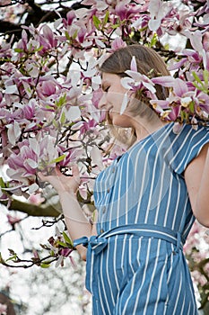 blonde with pleasure inhales an aroman of magnolia flowers standing under a tree