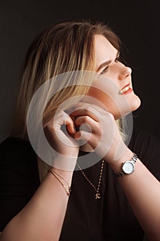 Blonde Plus Size Model on a black background in dark clothes, fastens the earring with two hands