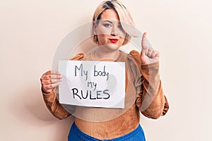 Blonde plus size woman asking for women rights holding paper with my body my rules message smiling with an idea or question