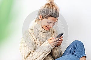 Blonde positive young woman smiling during playing the games on cellphone. Happy female chatting with her boyfriend, looking at