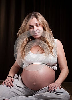 Blonde pregnant woman sitting and looking at camera