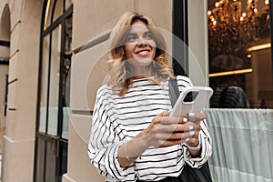 Blonde pretty woman holding phone and have chat loot away on the street