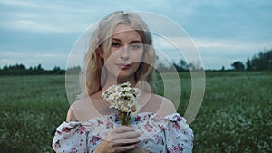 Blonde pretty woman holds a bouquet of daisies standing in the field