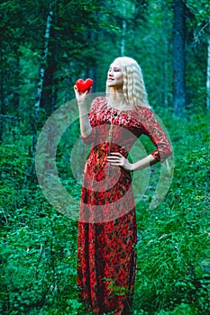 A blonde in a red dress with a red heart of thread in her hands
