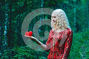 A blonde in a red dress with a red heart of thread in her hands