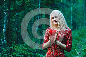 A blonde in a red dress with a red heart of thread in her hands