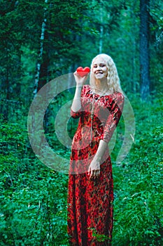 A blonde in a red dress with a red heart of thread in her hands