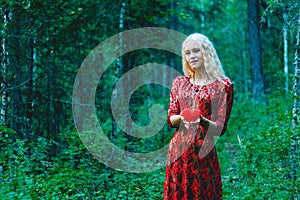 A blonde in a red dress with a red heart of thread in her hands