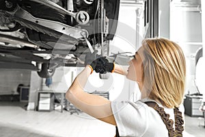 Blonde repairing auto undercarriage with wrench.