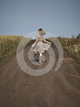 The blonde runs down a country road in a striped dress from the back