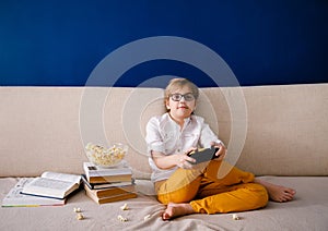 Blonde schoolboy boy plays video games, holds a gamepad, eats popcorn instead of learning lessons on blue background