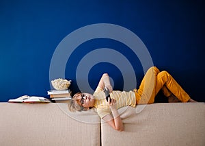 Blonde schoolboy boy plays video games, holds a gamepad, eats popcorn instead of learning lessons on blue background