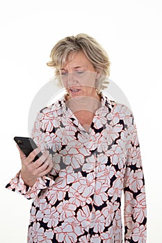 Blonde senior elderly woman looks screen of cell mobile phone in pink white blouse with pink flowers smartphone on white