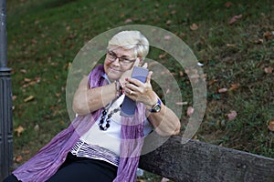 Blonde senior woman primps looking at cellphone on park bench