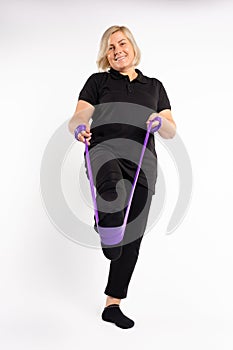 Blonde senior woman stretches elastic band with leg. Healthy, pandemic concept