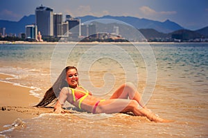 blonde slim girl in bikini lies on back in edge of sea smiles