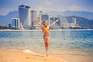 Blonde slim girl in bikini poses smiles on edge of azure sea