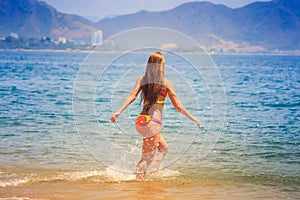 blonde slim girl in bikini runs into sea splashes against hills