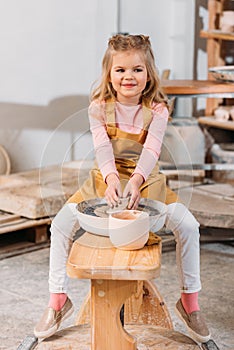 blonde smiling kid making ceramics on pottery wheel