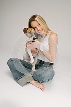 Blonde smiling pretty woman hugging dog Jack Russell terrier.