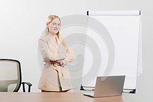 a blonde in a suit in an office with a board for meetings, desktop and laptop